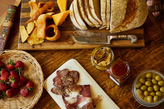 Planche de charcuterie avec pain, fromage, olives, confiture, fruits et chips, idéale pour un apéritif gourmand.