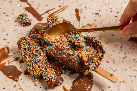 Bâtonnets au chocolat recouverts de vermicelles colorés sur une surface en marbre avec une cuillère dorée.