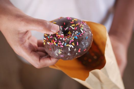 Bâtonnet au chocolat avec des vermicelles colorés, tenu dans une main, sortant d'un sac en papier.